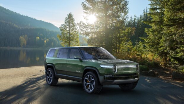 A Rivian electric SUV parked near a lake surrounded by tall pine trees at sunrise, 4K Desktop Wallpaper