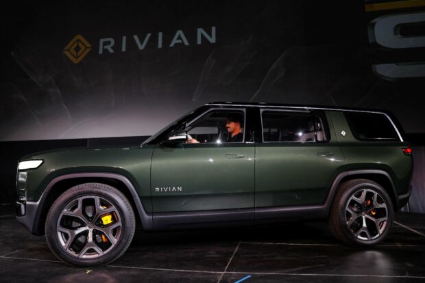 A green Rivian electric SUV with a person inside is shown on stage, HD Desktop Wallpaper