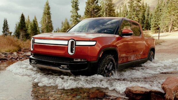 A Rivian automotive is driving through a shallow mountain stream surrounded by trees, HD Desktop Wallpaper
