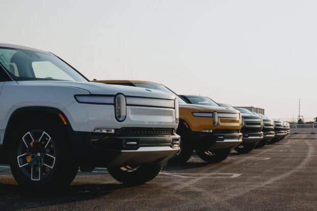 A lineup of Rivian electric trucks is parked outdoors under clear skies, 2K Desktop Wallpaper