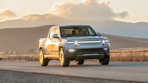 A Rivian pickup truck is driving on a desert road during sunset with mountains in the background, HD Desktop Wallpaper