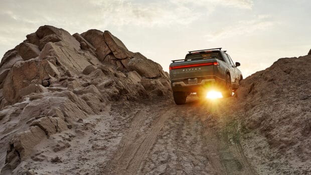 A Rivian Automotive vehicle is climbing a steep rocky trail at sunset, HD Desktop Wallpaper