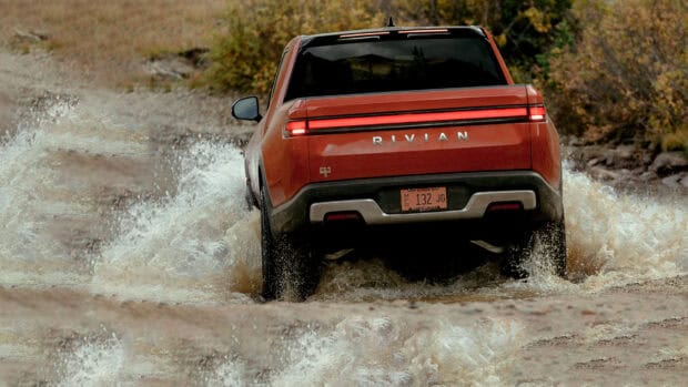 A red Rivian truck is driving through a shallow river crossing in the wilderness, HD Desktop Wallpaper