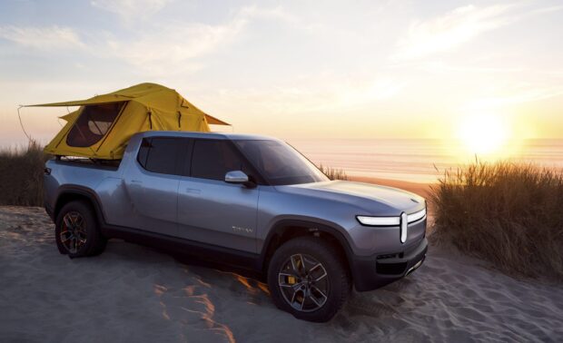 A Rivian Automotive Wallpapers truck is parked on a sandy beach with a yellow rooftop tent and sunset in the background, 2K Desktop Wallpaper
