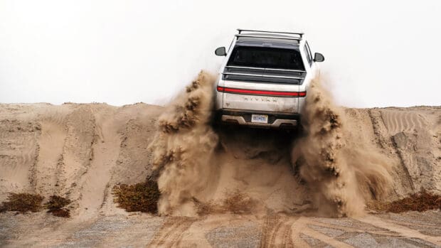A Rivian vehicle is kicking up sand while driving off road on a desert trail, HD Desktop Wallpaper