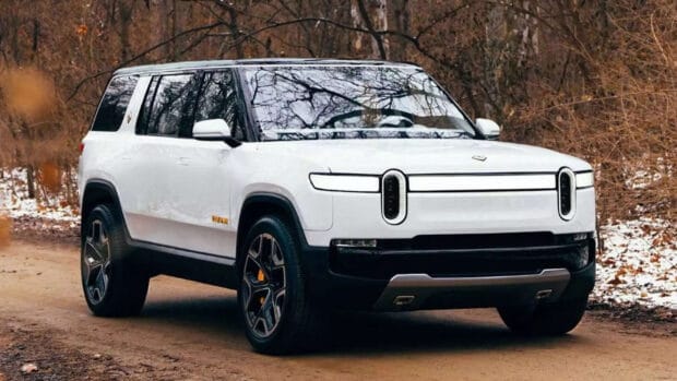A white Rivian automotive vehicle parked on a dirt road surrounded by autumn trees, HD Desktop Wallpaper