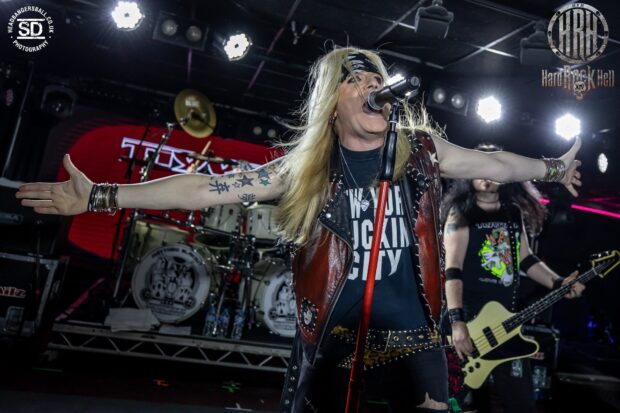 A rock band performs with an energetic lead singer wearing a leather vest and long hair at a live concert, HD Desktop Wallpaper