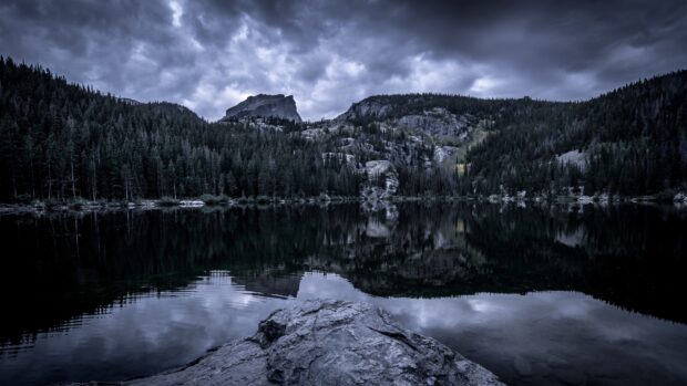 A calm lake reflects the cloudy sky and pine trees in Rocky Mountain National Park, 4K Desktop Wallpaper