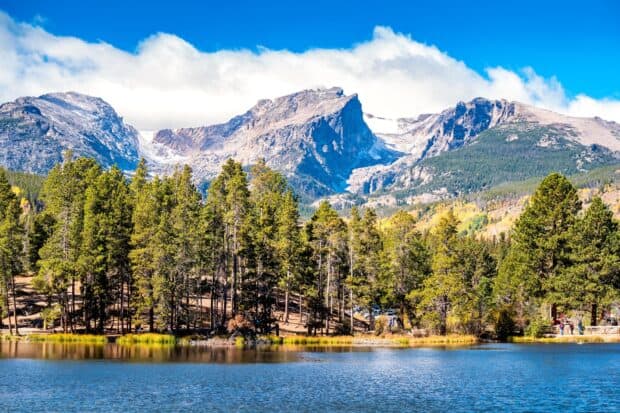 A clear lake reflects pine trees and rocky peaks in the Rocky Mountain National Park, HD Desktop Wallpaper