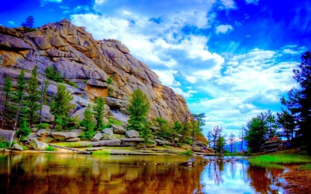 The Rocky Mountain National Park shows rocky cliffs and pine trees beside a calm reflective lake, HD Desktop Wallpaper