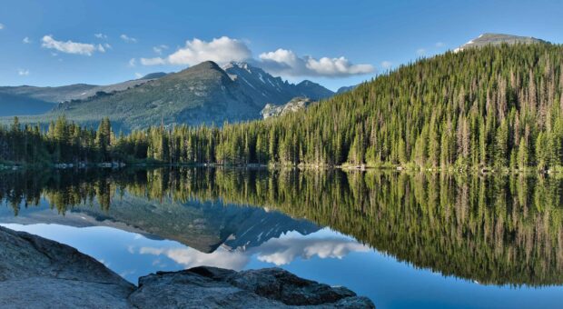 The Rocky Mountain National Park shows a clear lake reflecting trees and mountains, 2K Desktop Wallpaper
