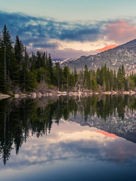 A peaceful lake reflects the pine trees and mountains in Rocky Mountain National Park, 2K Mobile Wallpaper