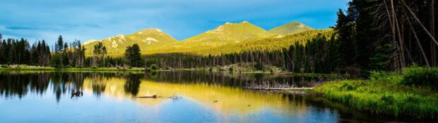 A peaceful lake reflects the Rocky Mountain National Park peaks and surrounding forest under a blue sky, 4K Desktop Wallpaper