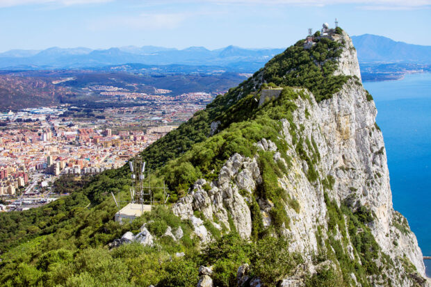 The photo shows the rugged cliffs of Gibraltar alongside the city and sea under a clear sky, 2K Desktop Wallpaper