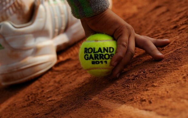 A tennis ball on a clay court with a player's hand ready for serve in a Roland Garros match, HD Desktop Wallpaper