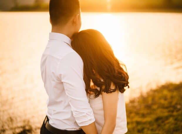 A couple embraces each other near a lake during golden hour with warm sunlight, HD Desktop Wallpaper