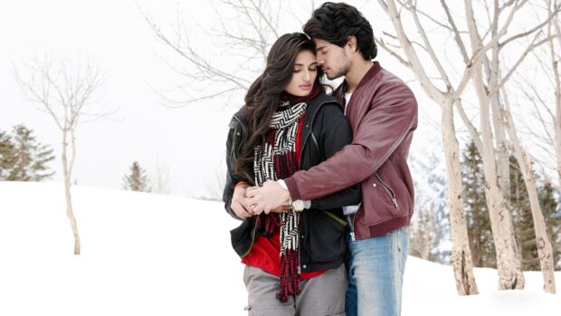 A romantic couple embracing tenderly in a snowy forest setting with bare trees and winter attire, HD Desktop Wallpaper