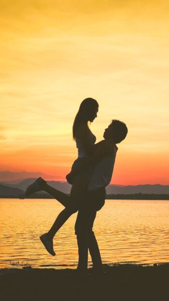 A love couple is sharing a joyful moment by the lake during a beautiful sunset, HD Mobile Wallpaper