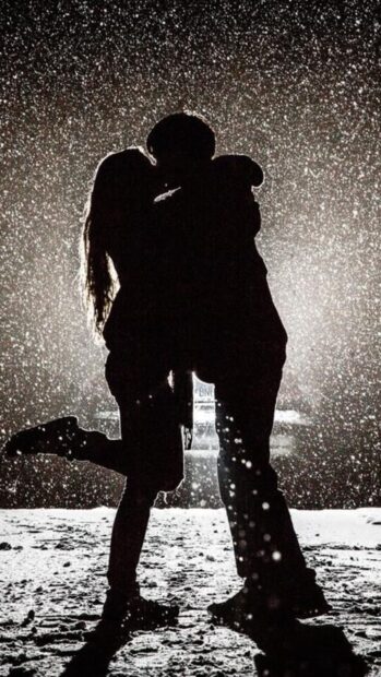 A love couple wallpapers silhouette shares a kiss under soft snowfall at night, 4K Mobile Wallpaper