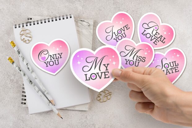 A hand holding a heart shaped sticker with love messages on a notebook, 2K Desktop Wallpaper