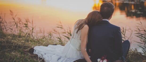 A love couple sits peacefully by the water at sunset with the woman resting her head on the man, 2K Desktop Wallpaper