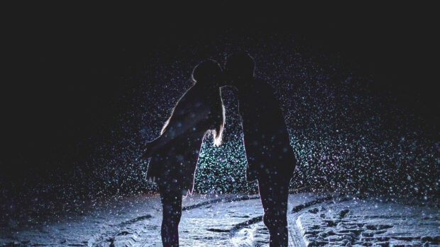 A love couple sharing a tender kiss under falling snow at night, 4K Desktop Wallpaper