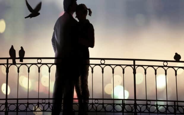A romantic couple silhouette stands close on a balcony with birds flying nearby, 2K Desktop Wallpaper