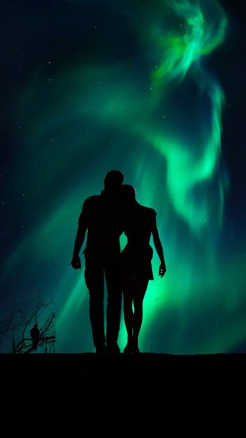 A couple embraces as the northern lights glow beautifully above them at night, 4K Phone Wallpaper
