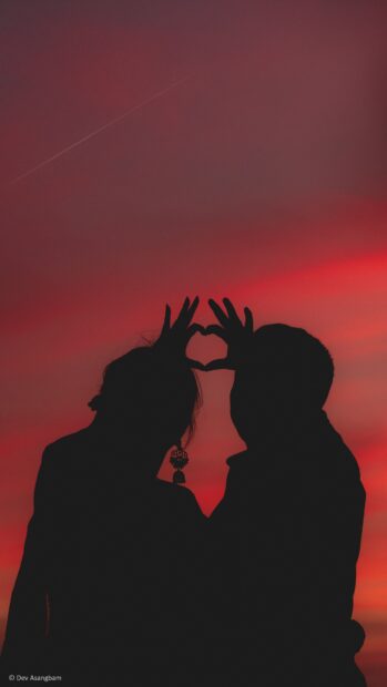 A couple creates a heart shape with their hands against a red sunset sky in love couple wallpapers, 4K Mobile Wallpaper