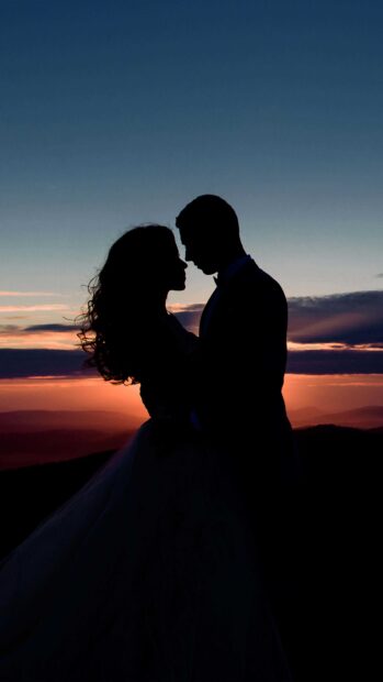 A love couple stands close together embracing under a colorful sunset sky, 4K Mobile Wallpaper