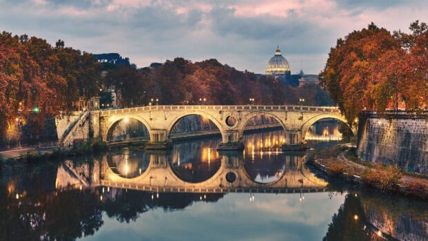 The Rome skyline shows a glowing bridge and autumn trees reflecting in the river, 4K Desktop Wallpaper