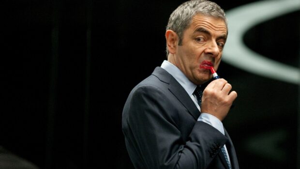 Rowan Atkinson applying red lipstick in a suit with a serious expression, 4K Desktop Wallpaper