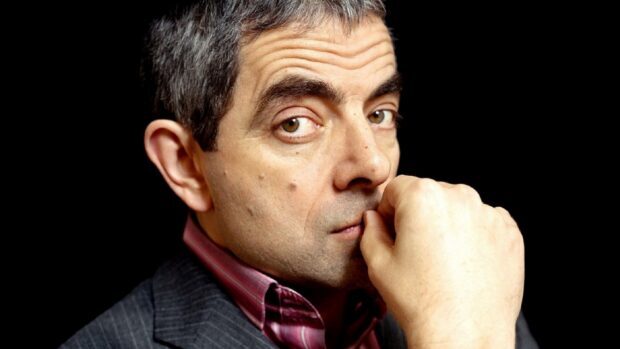 Rowan Atkinson looks thoughtfully into the camera with a black background, 4K Desktop Wallpaper