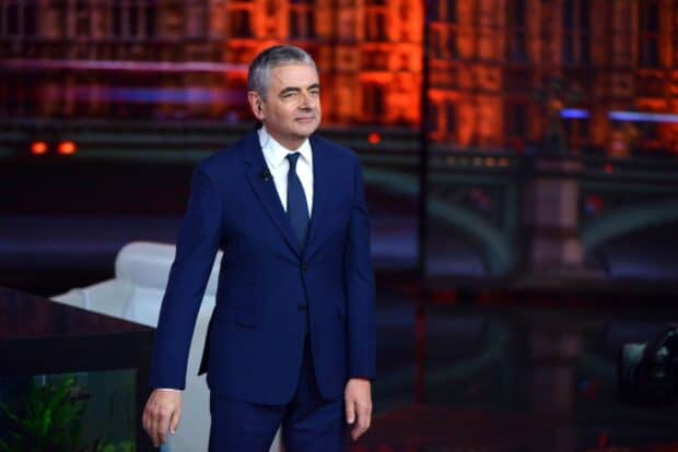 Rowan Atkinson is standing in a studio wearing a formal blue suit and tie, HD Desktop Wallpaper