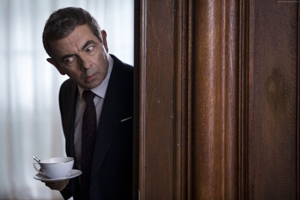 Rowan Atkinson is cautiously peeking from behind a wooden door holding a cup, 2K Desktop Wallpaper