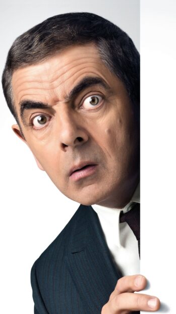 Rowan Atkinson shows a surprised expression peeking from behind a white wall, 2K Phone Wallpaper