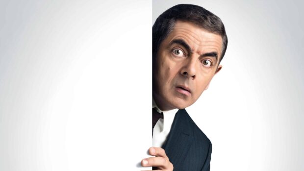 Rowan Atkinson peeks around a white wall wearing a dark suit with a surprised expression, 4K Desktop Wallpaper