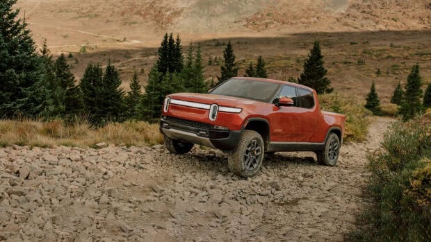 A red Rivian Automotive vehicle climbs rocky terrain in a forested mountain area, HD Desktop Wallpaper