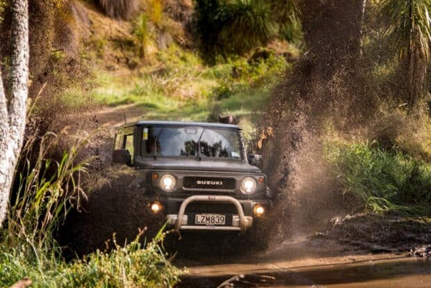 A Suzuki vehicle is captured driving through mud and spraying water in an off road driving scene, HD Desktop Wallpaper