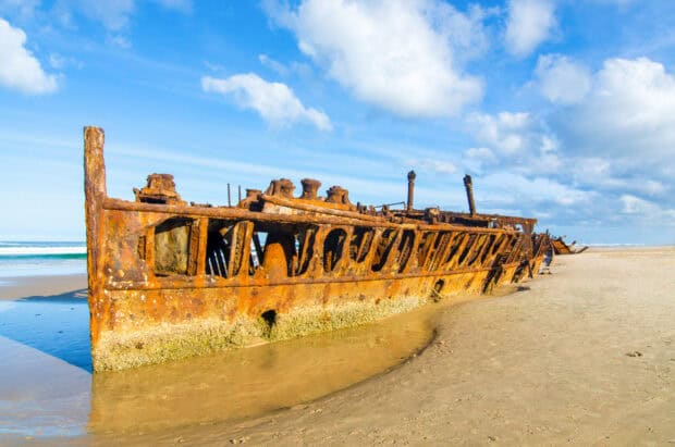 The rusty shipwreck rests on the sandy beach of Fraser Island under a blue sky with clouds, HD Desktop Wallpaper