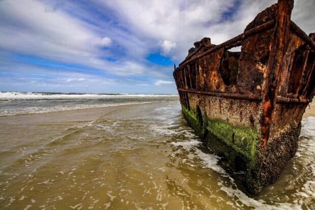 A rusty shipwreck covered with moss rests on the shore of Fraser Island under a cloudy sky, HD Desktop Wallpaper