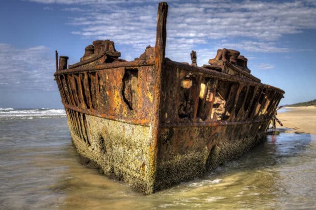 A rusty shipwreck stands on the sandy shore of Fraser Island with waves nearby, HD Desktop Wallpaper