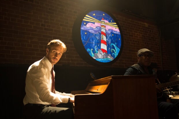 Ryan Gosling plays the piano in a dimly lit room with a stained glass lighthouse window, 2K Desktop Wallpaper