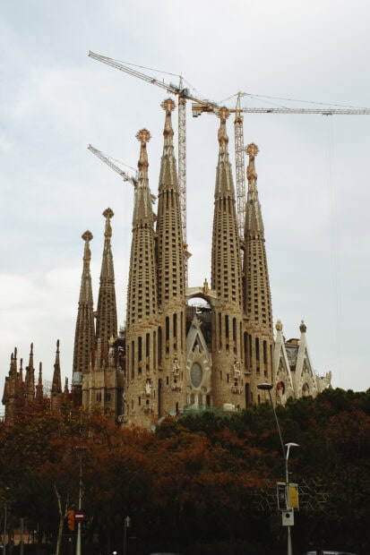 The Sagrada Familia towers stand tall with cranes against a cloudy sky, 2K Mobile Wallpaper