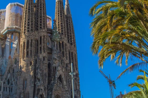 The Sagrada Familia shows intricate architecture under a clear blue sky with nearby palm trees, 2K Desktop Wallpaper