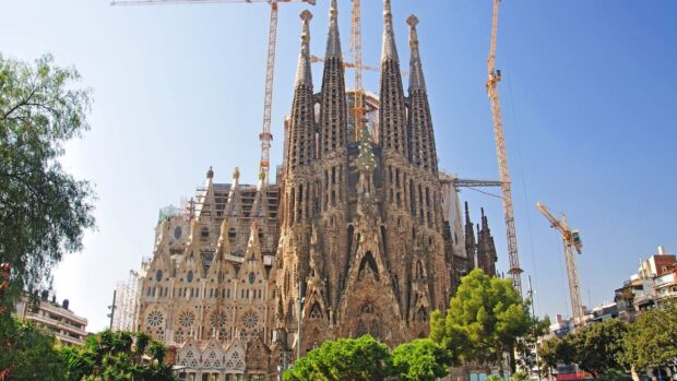 The Sagrada Familia cathedral towers rise tall with construction cranes around, 2K Desktop Wallpaper