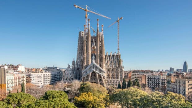 The Sagrada Familia stands tall among city buildings under a clear blue sky, HD Desktop Wallpaper