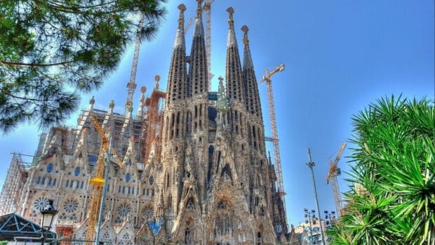The Sagrada Familia stands tall under a clear blue sky with cranes in the background, 4K Desktop Wallpaper