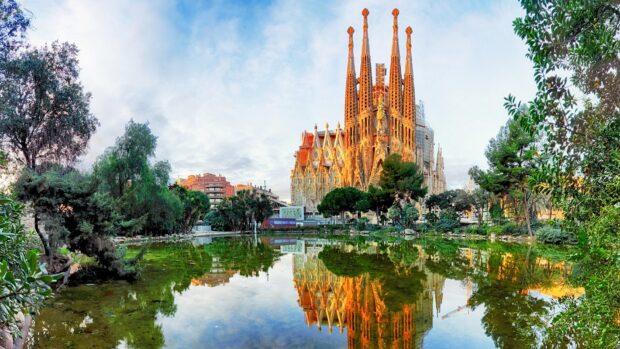 The Sagrada Familia is reflected in a calm pond surrounded by trees at sunrise, HD Desktop Wallpaper