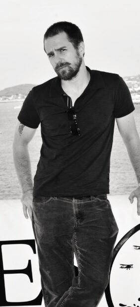 Sam Rockwell stands casually outdoors near the sea with a serious expression, 2K Mobile Wallpaper